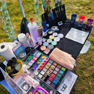 Stand maquillage artistique en plein air avec pinceaux, fards colorés, paillettes et matériel professionnel.