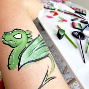 Dessin de dragon vert réalisé en bodypainting sur la cuisse, avec matériel de maquillage artistique en arrière-plan.