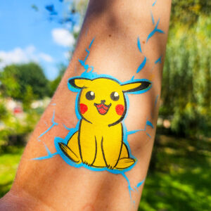 Maquillage enfant représentant Pikachu avec des éclairs bleus, réalisé sur l’avant-bras et photographié en extérieur par une journée ensoleillée.