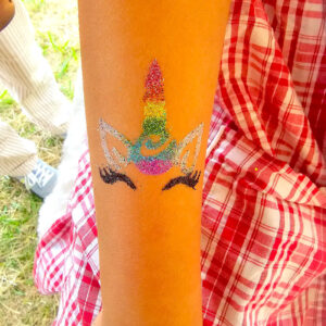 Tatouage éphémère en paillettes représentant une licorne arc-en-ciel sur l’avant-bras d’un enfant.
